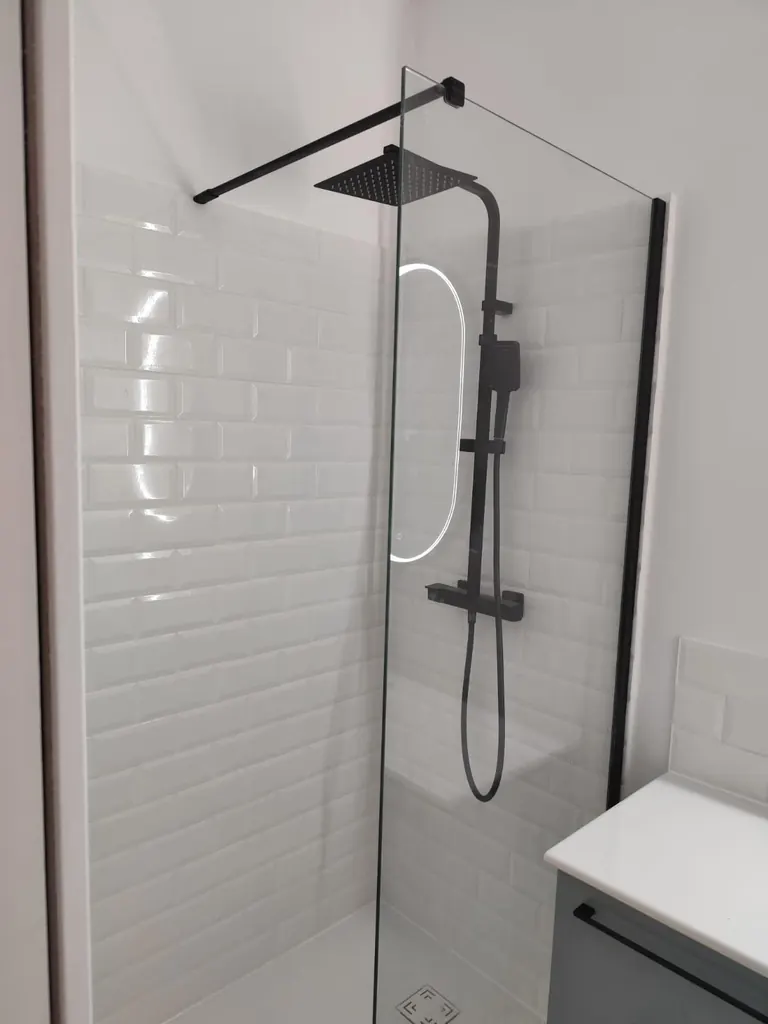 Douche terminée : faïence métro blanche, paroi vitrée et colonne de douche noire