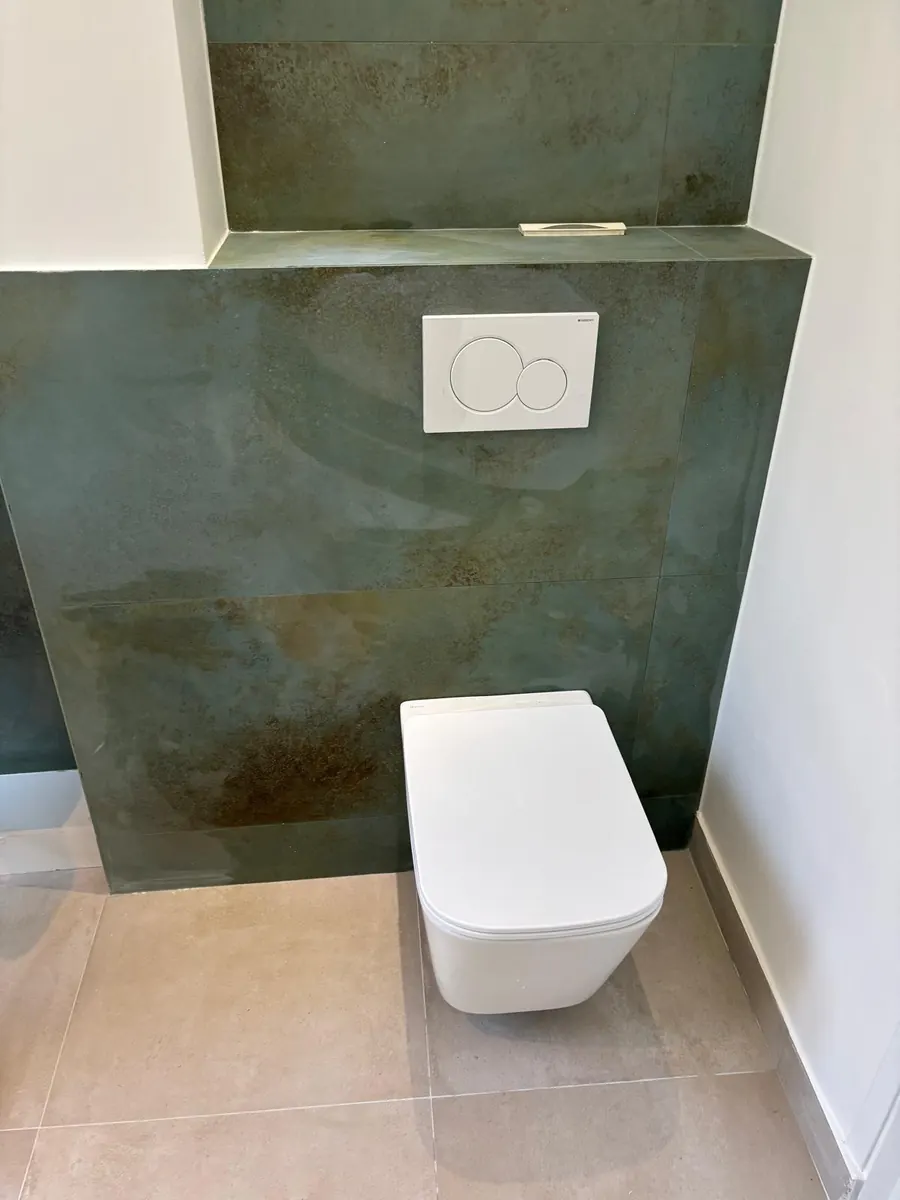 Toilettes terminées : WC suspendu blanc, plaque de commande, faïence verte grand format et sol beige